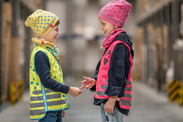 Junge und Mädchen stehen sich gegenüber mit reflektierender Warnweste und Mütze
