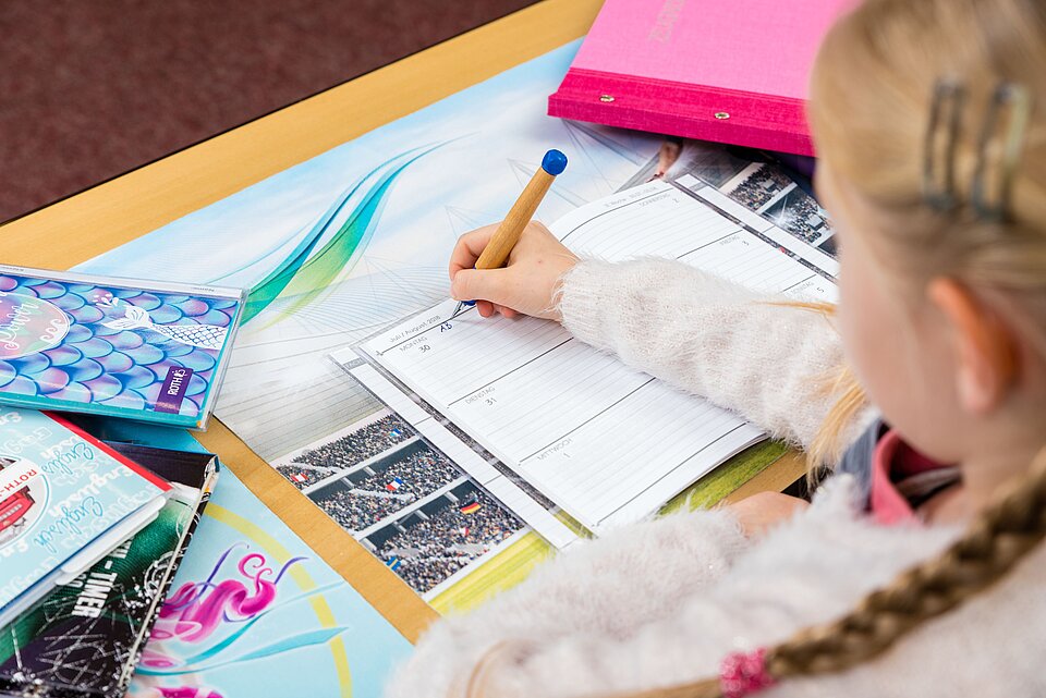 Kind schreibt am Schreibtisch in ein Hausaufgabenheft